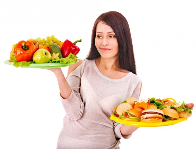 Eine Frau hält ein Teller mit gesundem Essen und eines mit Junkfood