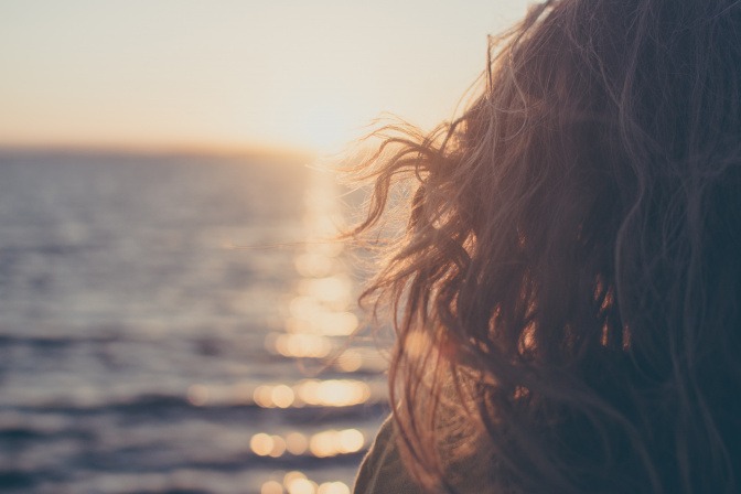 Eine Frau mit langen Haaren sitzt am Meer