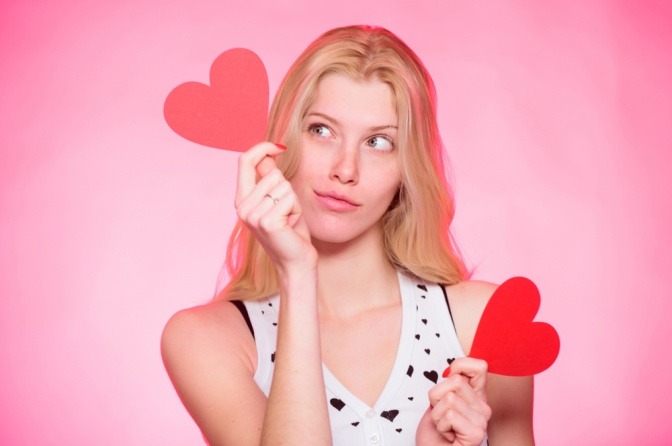 Eine Frau hält rote Valentinsherzen in der Hand und wirkt nachdenklich.