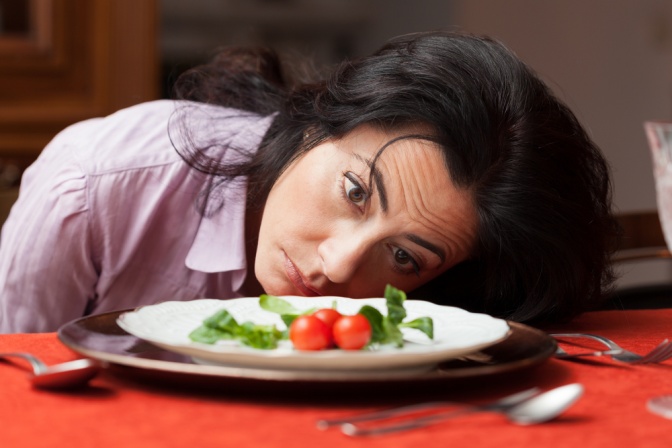 Eine Frau liegt mit traurigem Kopf vor einem Teller 