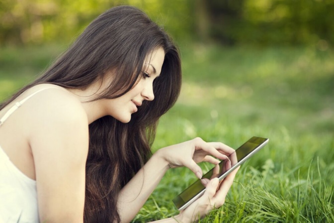 Eine Frau liegt in der Wiese und liest am Ipad