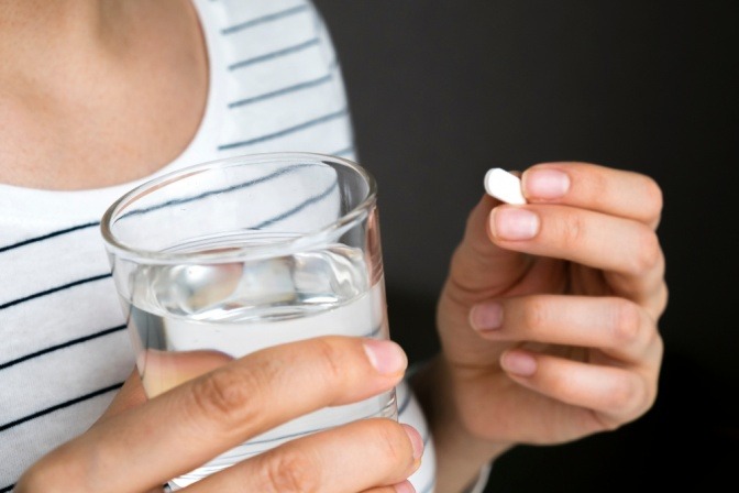 Eine Frau nimmt eine Tablette gegen den Kopfschmerz zu sich