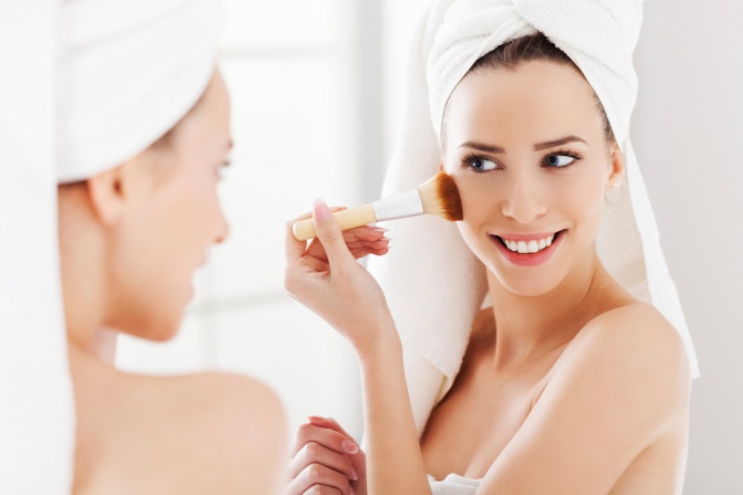 Eine Frau trägt mit einem Make up Pinsel ein Tages Make up vor einem Spiegel auf