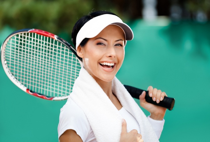 Frau mit Tennisschläger über der Schulter lächelt glücklich in die Kamera