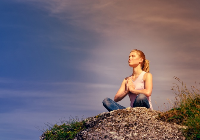 Eine Frau sitzt auf einem Stein und übt Yoga aus.