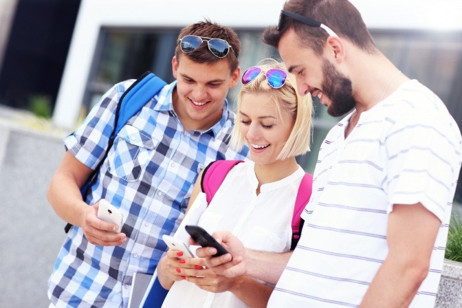 Eine Frau und zwei Männer schauen auf den Bildschirm ihrer Smartphones
