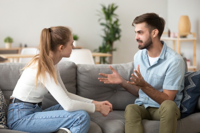 Junger Mann und junge Frau sitzen auf einem Sofa und führen ein ehrliches Gespräch.