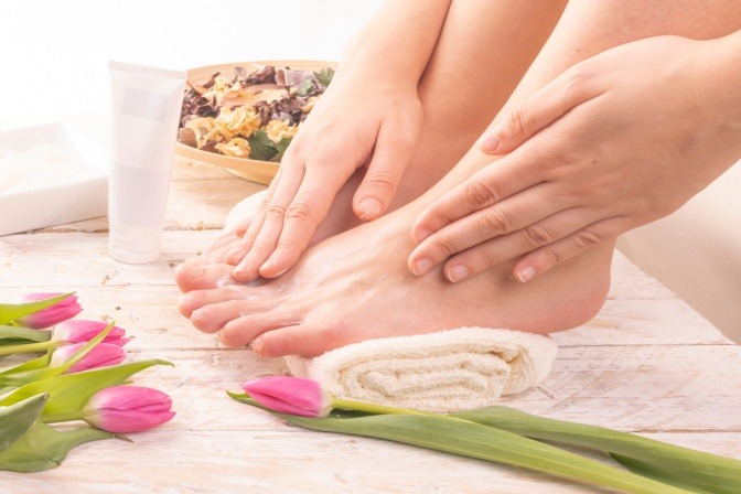 Frau verwöhnt ihre Füße mit einer Massage und einer Creme