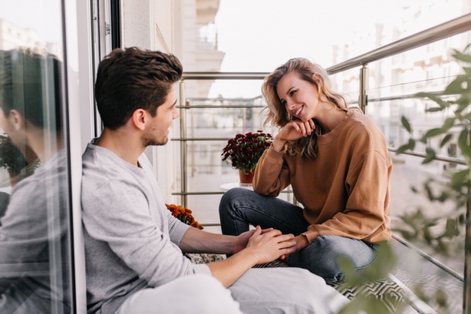 Ganzheitliche Kommunikation - junges Paar auf Balkon, er hält ihre Hand beim Gespräch. 