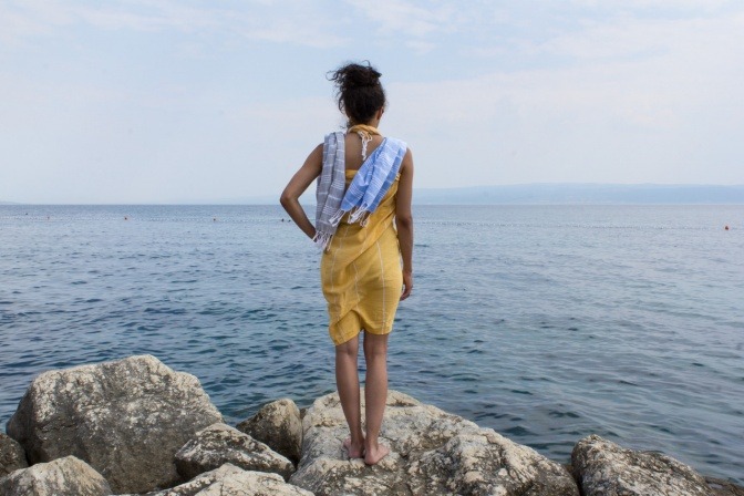 Frau mit einem gebundenen Tuch am Meer auf einem Felsen