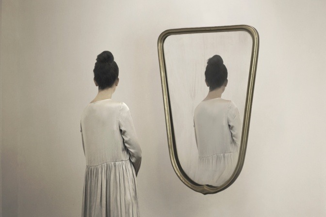 Frau steht vor einem Spiegel und wendet sich von ihrem Spiegelbild ab.