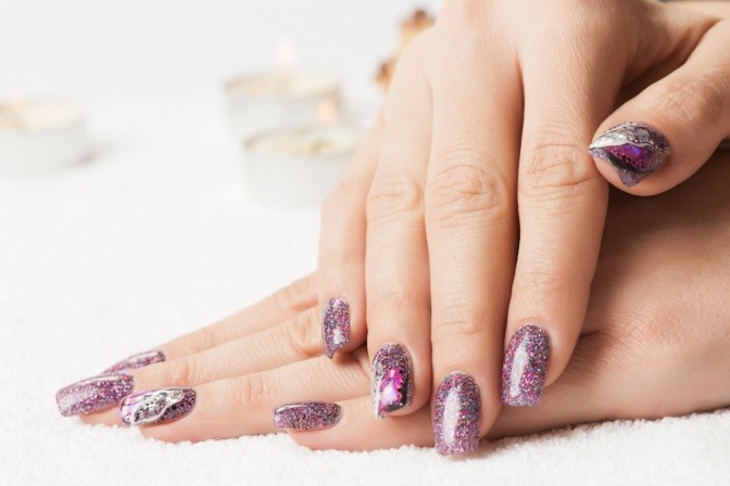 Eine Frau trägt glitzernde Gelnägel in einem violetten Farbton