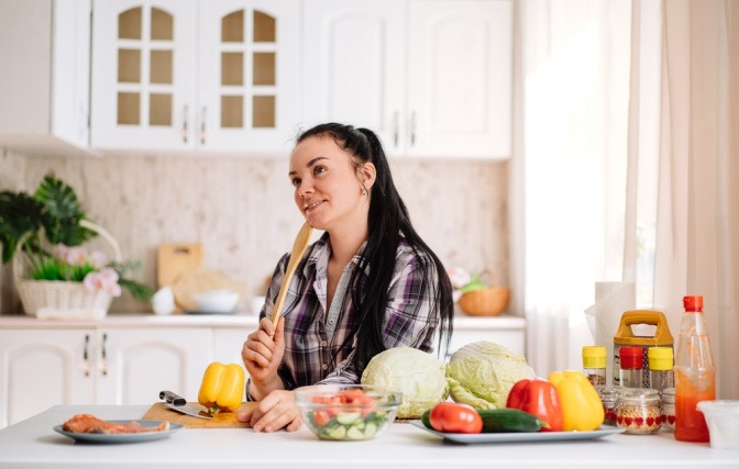 Frau in Küche überlegt, welches Gemüse sie fermentieren soll. 