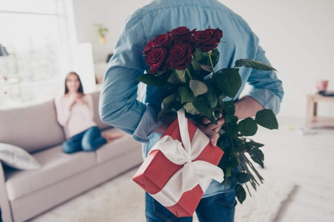 Ein Mann versteckt hinter seinem Rücken Rosen und ein Geschenk