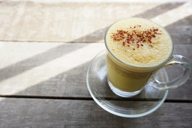 Glas mit goldener Milch auf einem Holztisch.