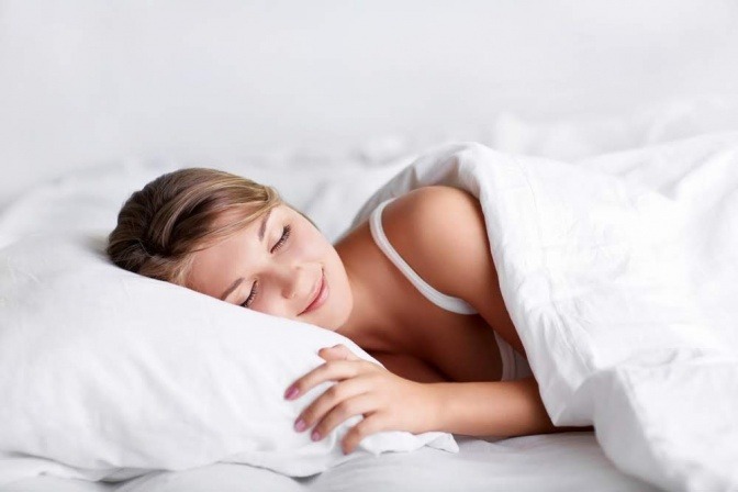 Eine Frau liegt schlafend in Seitenlage im Bett und träumt offensichtlich etwas Schönes, denn sie hat ein leichtes Lächeln im Gesicht.