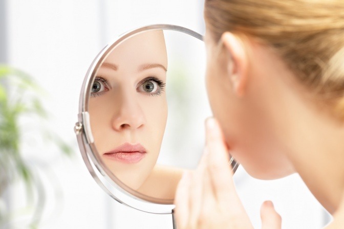 Eine Frau mit glänzender Haut schaut in den Spiegel