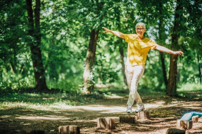 Eine ältere Frau balanciert auf abgesägte Baumstämmen