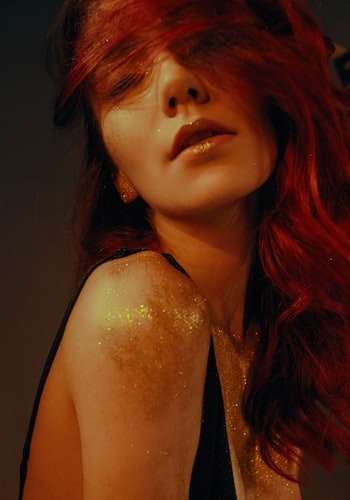 Eine rothaarige Frau trägt im Gesicht und am Körper goldenen Glitter