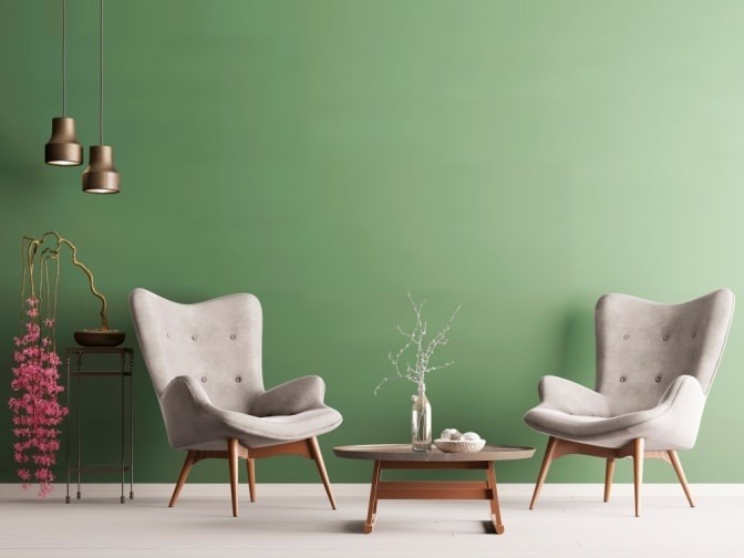 Vor einer grünen Wand stehen zwei Stühle und ein Tisch