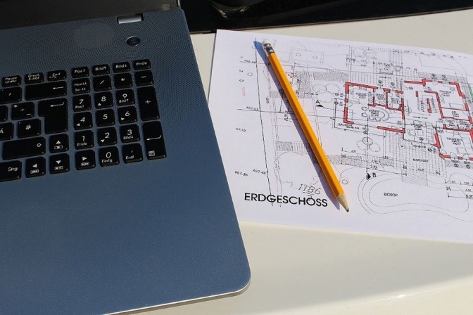 Neben einem Laptop liegt ein Grundriss-Plan