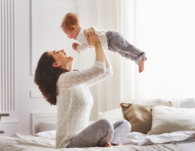 Frau mit guter Figur hält glücklich Baby in die Höhe