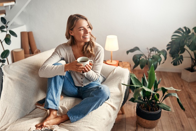 Frau trinkt eine Tasse Tee auf dem Sofa und lächelt