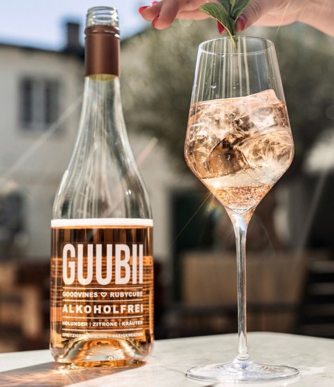 Flasche alkoholfreier GUUBII, daneben ein gefülltes Glas mit Eiswürfeln