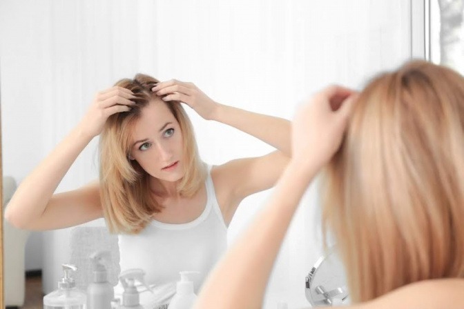 Eine blonde Frau betrachtet ihren dunklen Haaransatz