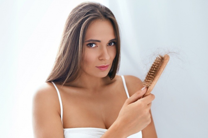 Eine verwunderte Frau blickt auf eine Haarbürste mit vielen Haarrückständen darin.