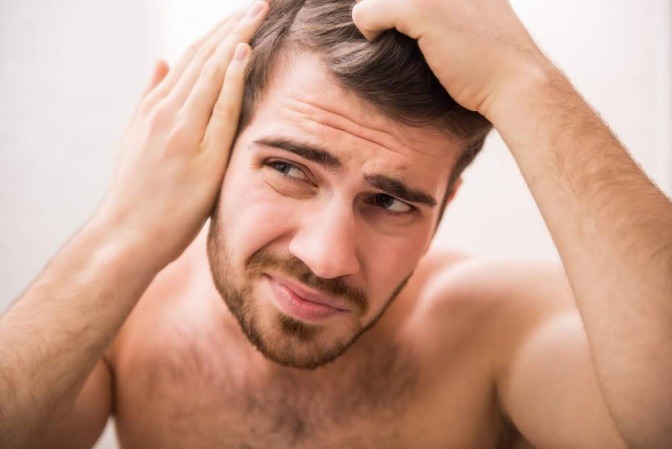 Mann betrachtet seine Haare kritisch vor dem Spiegel.