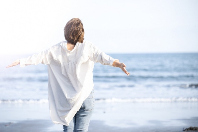 Eine Frau in den Wechseljahren breitet am Meer die Arme aus