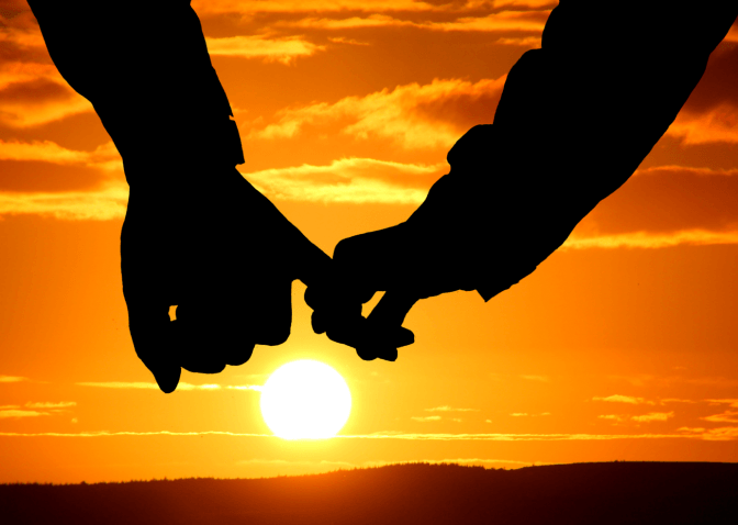 Zwei Hände halten sich bei Sonnenuntergang