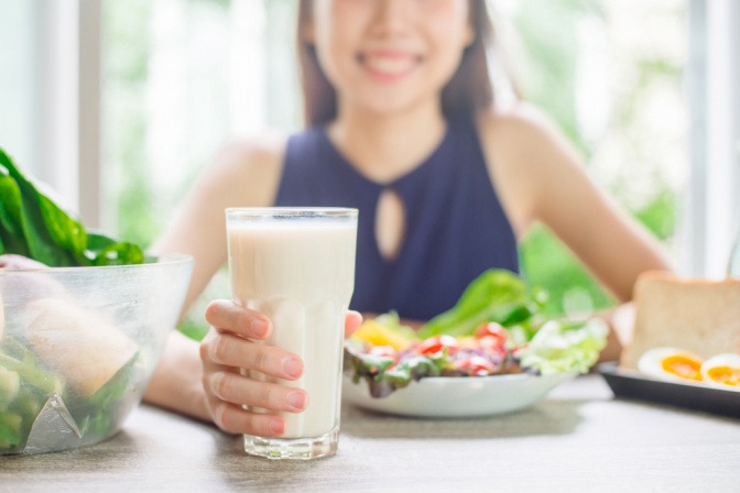 Frau isst Salat und trinkt Hafermilch.