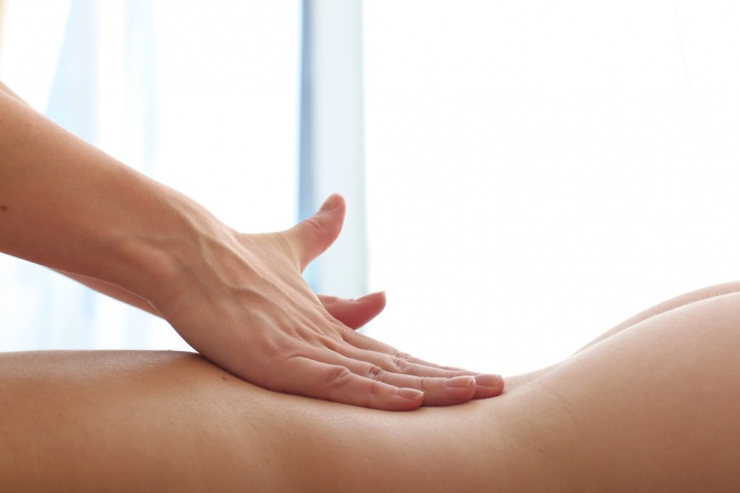 Eine Hand massiert bei einer erotischen Massage einen nackten Rücken