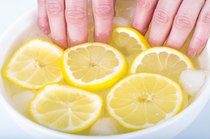 Frau nimmt ein Handbad mit Zitronenscheiben für Nagelpflege