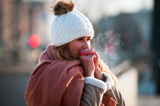 Eine junge Frau pustet im Winter ihre Hande wärm