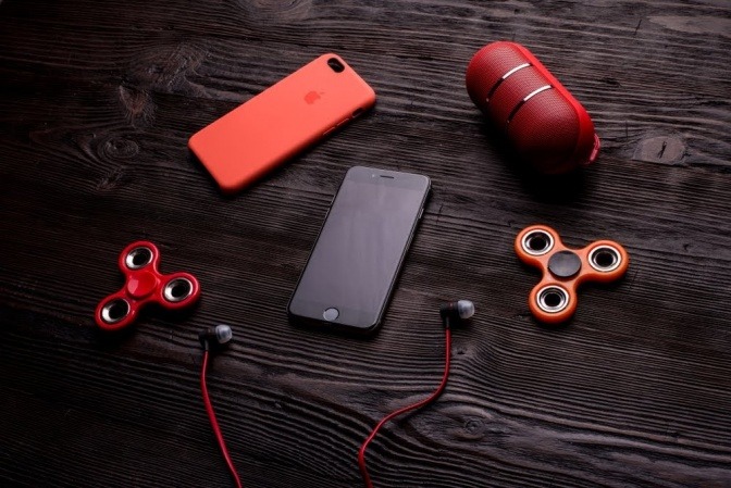 Ein Smartphone und diverse Gadgets wie Kopfhörer und Bluetooth-Lautsprecher liegen auf einem Holztisch.