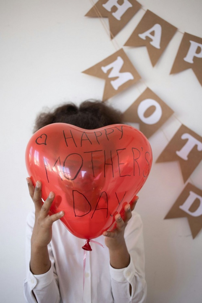 Ein Kind hält einen Ballon, auf dem "Happy Mother's Day" steht