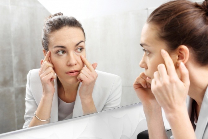 Eine Frau betrachtet ihre Haut, die Regeneration braucht, im Spiegel