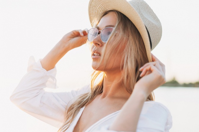 Frau mit Sonnenbrille und Sonnenhut gegen Hautalterung
