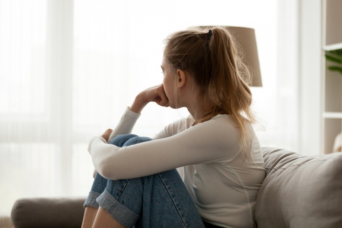 Eine nachdenkliche junge Frau mit Hemmungen sitzt auf der Couch