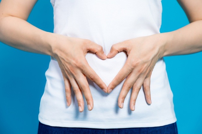 Auf dem Foto sieht man eine Frau, die mit ihren Fingern  unter ihrem Bauchnabel ein Herz formt. 