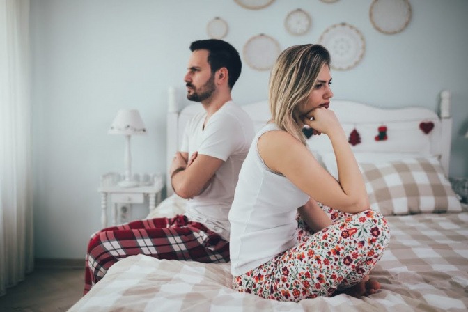 Ein Paar hat sich gerade gestritten und sitzt nun, jeweils mit dem Rücken zum anderen Partner, auf dem Bett.