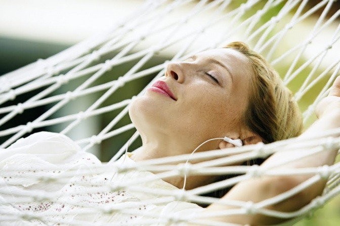 Eine Frau liegt in einer Hängematte und lässt sich die Sonne auf das Gesicht scheinen. Sie wirkt zufrieden, entspannt und glücklich.