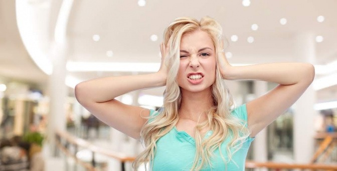 Eine junge Frau steht in der Halle eines Einkaufszentrums. Sie hat die Hände über ihrem Kopf verschränkt und wirkt gestresst.