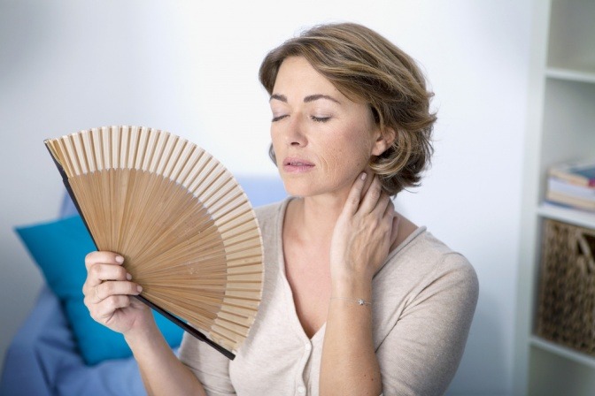 Eine Frau hält einen Fächer wegen der Hitzewallungen durch Hormone (Wechseljahre)