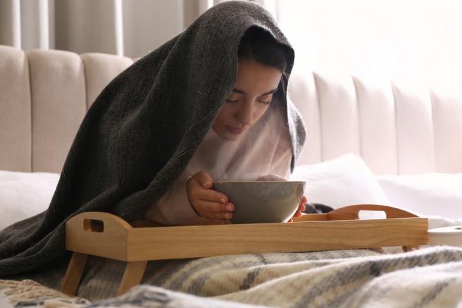 Eine Frau macht eine Dampftherapie mit ätherischen Ölen in ihrem Bett.
