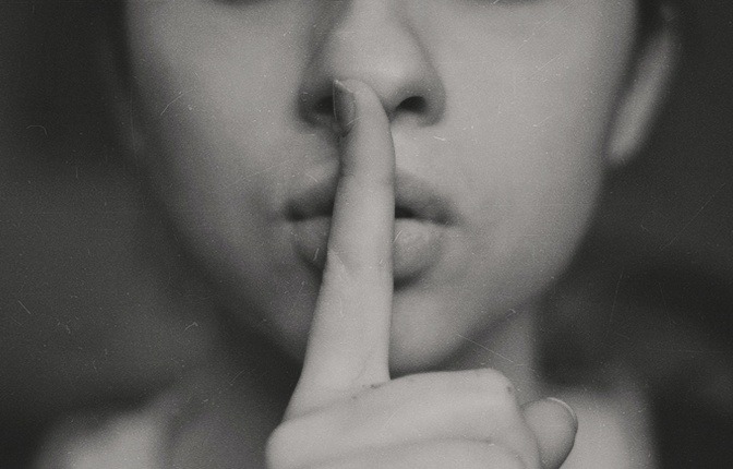 Eine Frau macht die typische Geste für das Stillsein, indem Sie einen Zeigefinger vor Ihren Mund hält. 