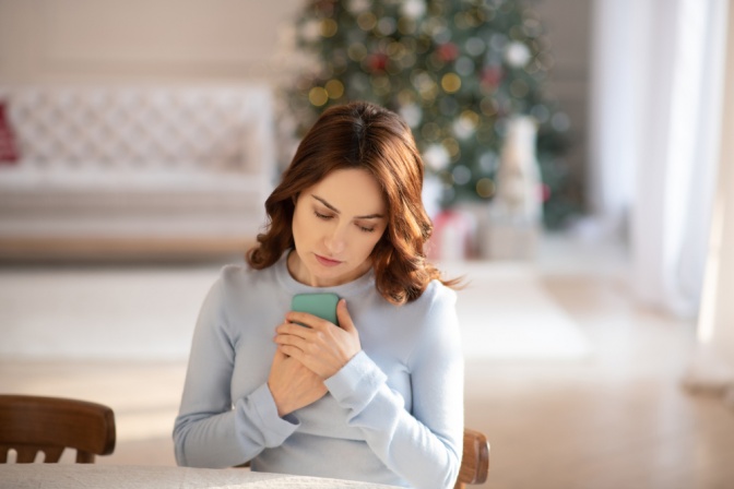 Nachdenkliche Frau hält ihr Smartphone an die Brust. 